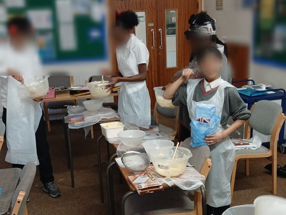 Students in aprons mixing cake batter during a cooking session, faces obscured