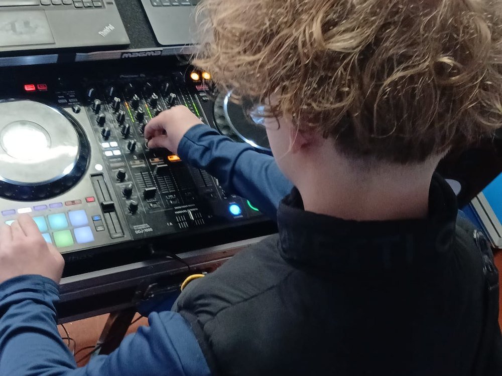 A student mixing on a DJ controller, hands on the faders, with track software open on a laptop behind