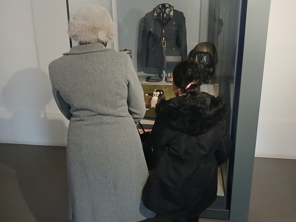 Two visitors looking at an RAF uniform and gas mask in a museum display case