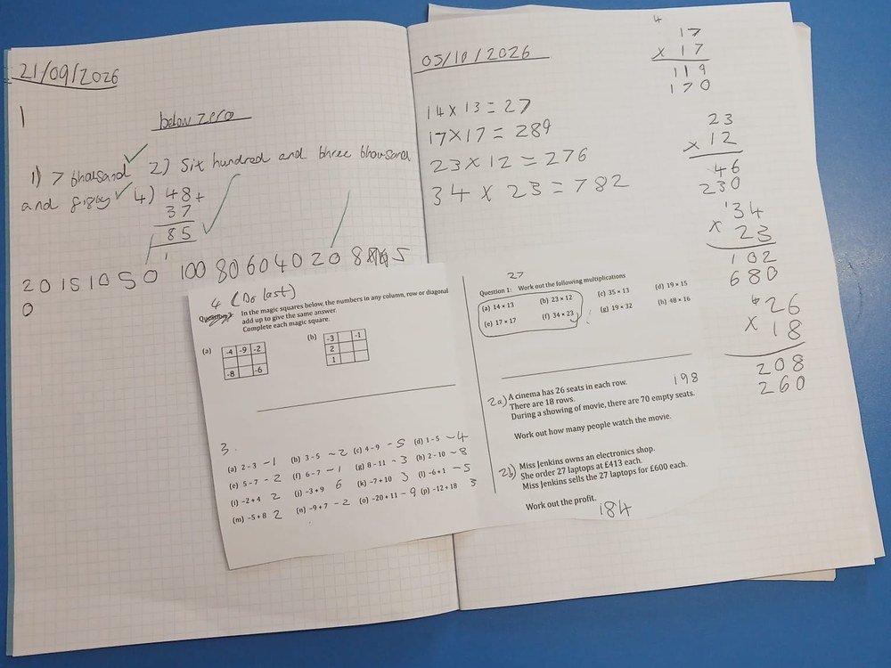 Exercise book pages showing long multiplication alongside a worked problem sheet