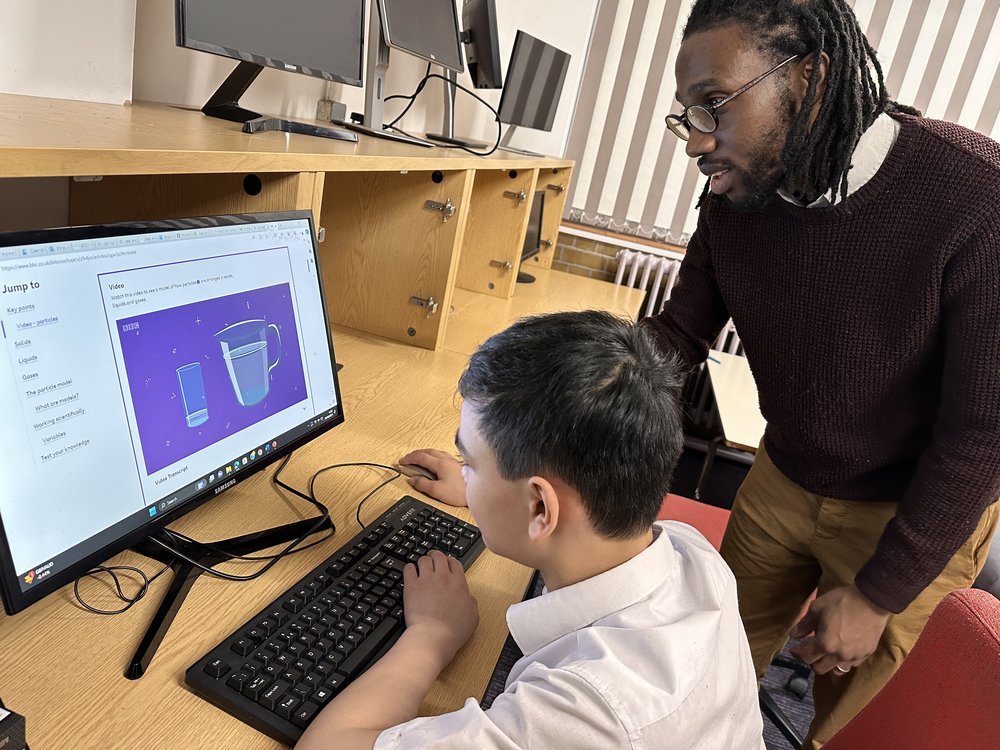 A student working through a BBC Bitesize page on solids, liquids and gases, with a member of staff alongside